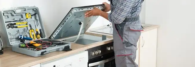 Cooktop repair technician lifting a built-in stovetop for service in Stamford, CT