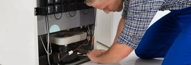 Refrigerator repair technician servicing the compressor and condenser area in Stamford, CT