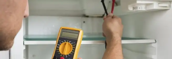 Refrigerator repair technician testing electrical components with a multimeter in Stamford, CT